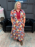 Woman wearing a floral maxi midi dress standing in a room with black leather chairs and a gray wall.