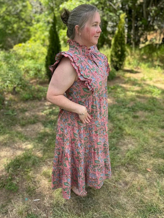 Woman in a floral dress standing outdoors with greenery in the background