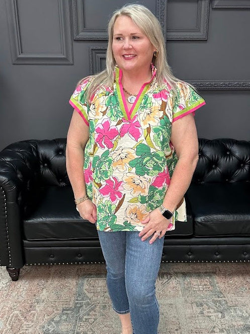 Woman wearing a colorful floral blouse and jeans standing in front of a black leather couch.