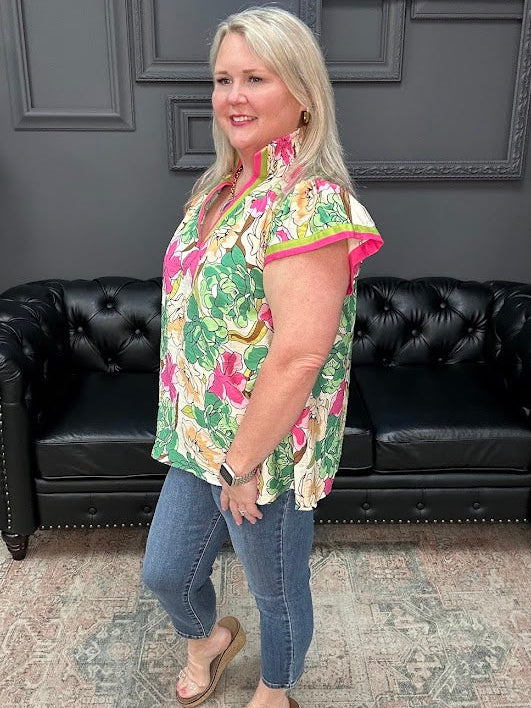 Woman wearing a floral shirt and jeans standing in front of a black leather couch.