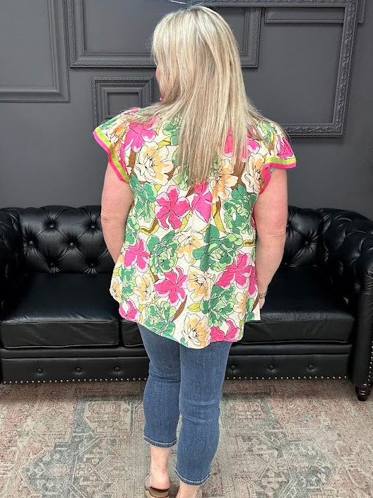 Person wearing a colorful floral top and blue jeans standing in front of a black leather couch.