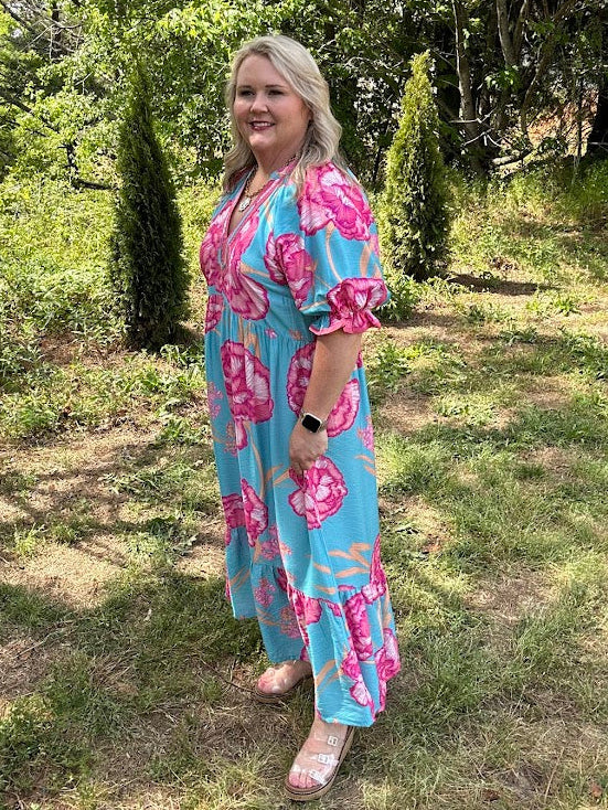 Woman in a blue and pink floral dress standing in a garden.
