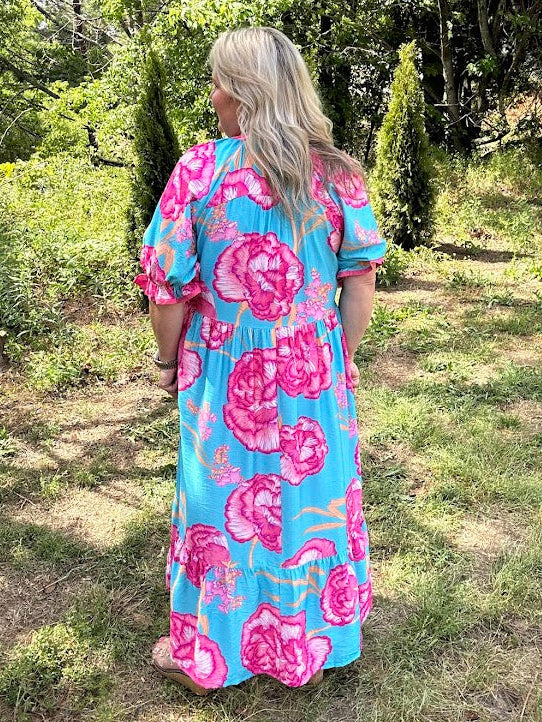 Woman wearing a blue and pink floral dress standing in a garden.