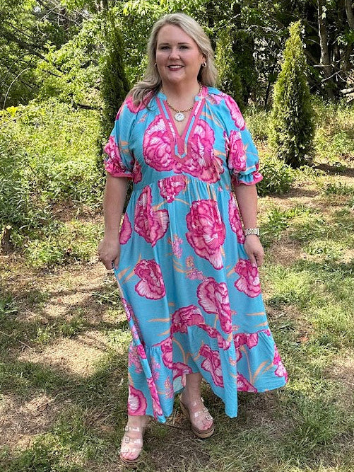 Woman wearing a blue and pink floral dress standing in a garden.