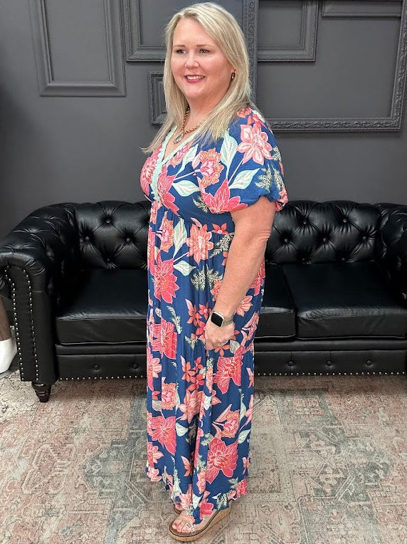 Woman in a floral dress standing in a room with a black leather couch and gray walls.