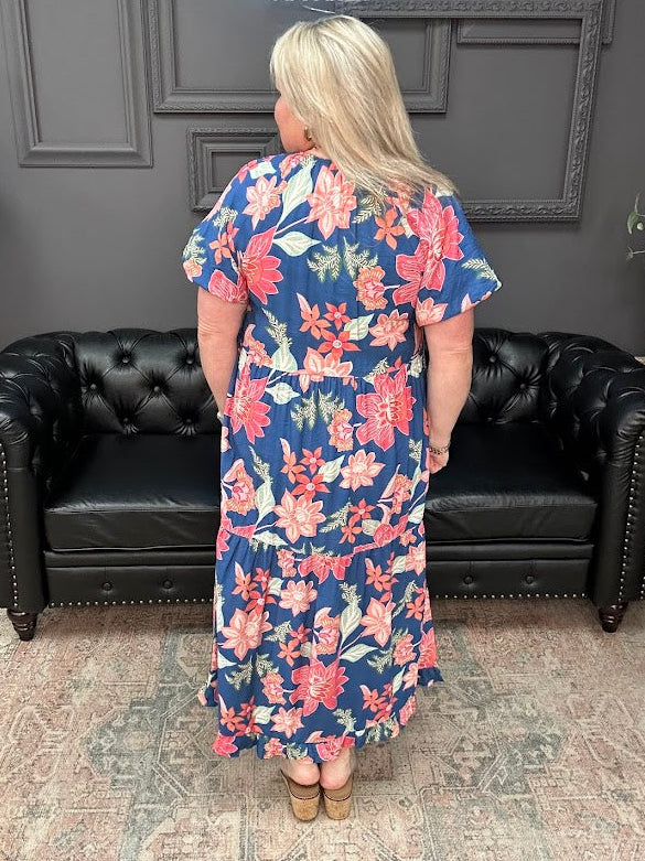Woman wearing a floral dress standing in a room with a black leather couch and gray walls.
