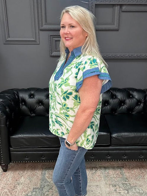 Woman wearing a green and white patterned shirt with blue accents in a room with a black leather couch.