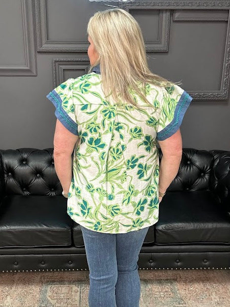 Woman wearing a green floral blouse and blue jeans standing in front of a black leather couch.