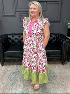 Woman wearing a floral dress with a pink top and green bottom in a room with black leather couches and gray walls.