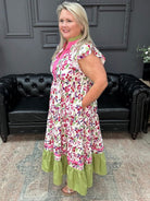 Woman wearing a floral dress with green ruffle hem in a room with black leather couches and gray walls.