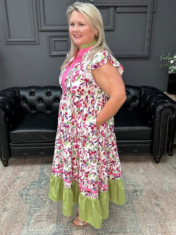 Woman wearing a floral dress with green ruffle hem in a room with black leather couches and gray walls.