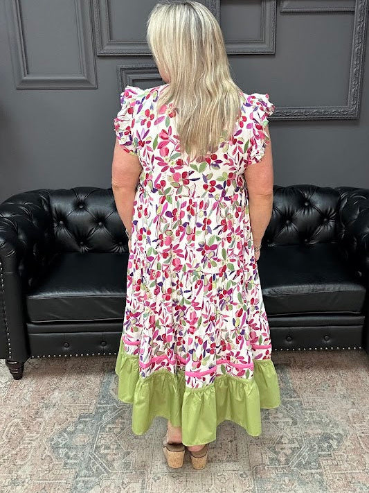 Woman wearing a floral dress with green hem in a room with black leather couches and gray walls.