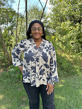 Person wearing a floral blouse standing outdoors with greenery in the background