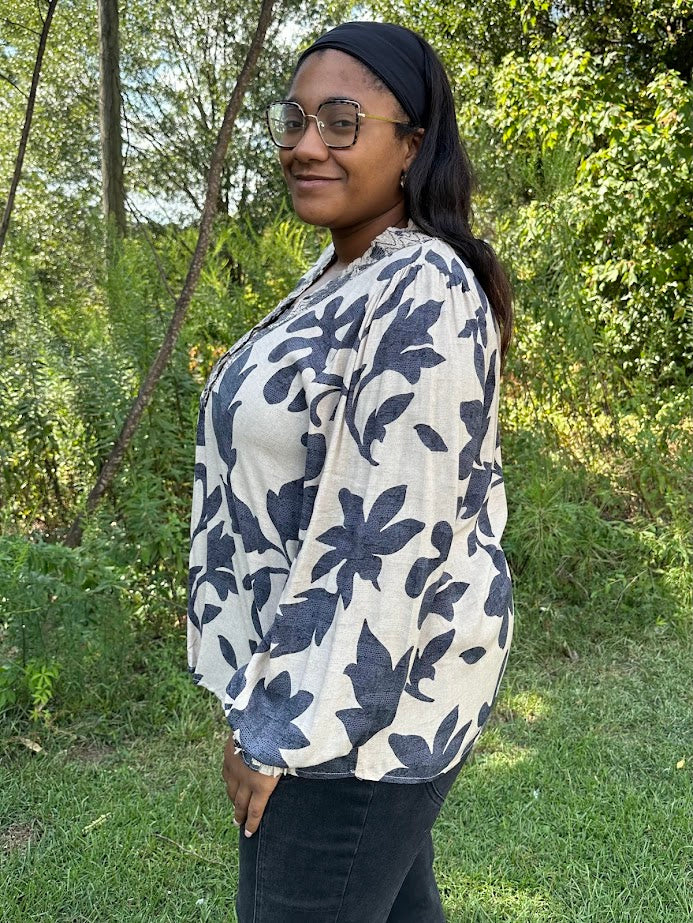 Woman wearing a floral blouse outdoors with greenery in the background
