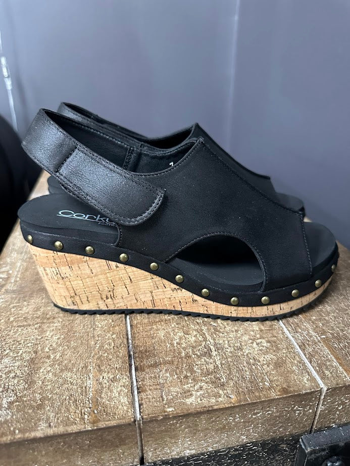 Black wedge sandal with cork sole on a wooden surface