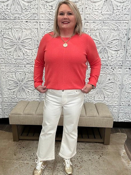 Woman in a coral shirt and white pants standing in front of decorative wall panels.