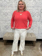 Woman in a coral shirt and white pants standing in front of decorative wall panels.