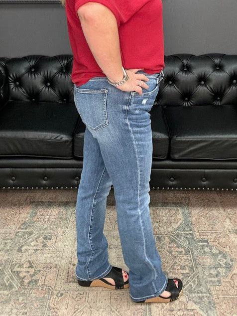Woman in a red shirt and blue jeans standing in front of black leather couches.