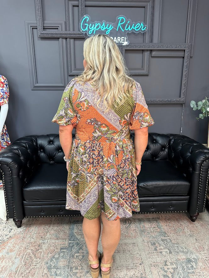 Woman wearing a patterned dress standing in front of a black leather couch with 'Gypsy River' branding.