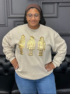 Person wearing a beige sweatshirt with gold graphics in front of a gray wall with 'Gypsy River Apparel' sign.