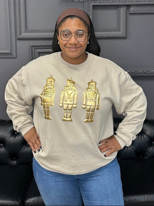 Person wearing a beige sweatshirt with gold graphics in front of a gray wall with 'Gypsy River Apparel' sign.