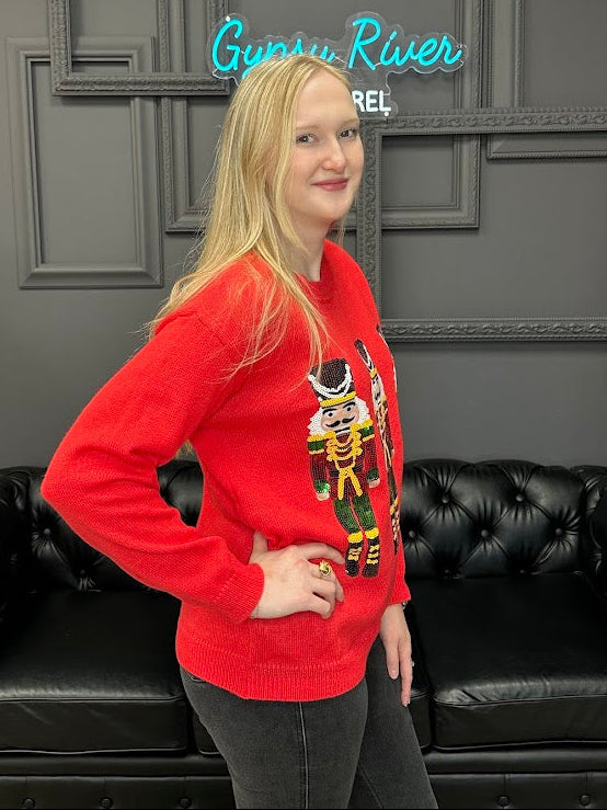 Person wearing a red sweater with a graphic design in a room with a black couch and gray walls.