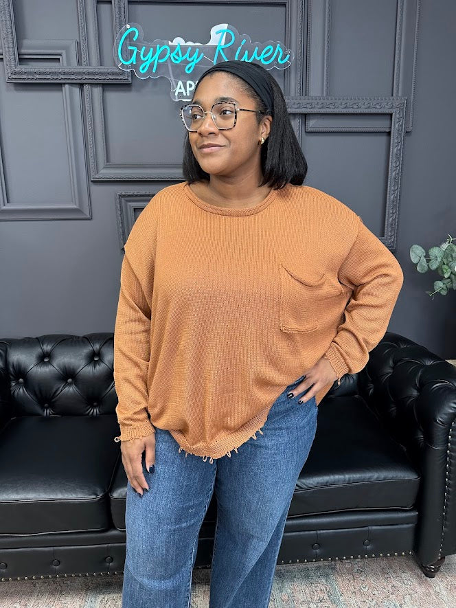 Woman wearing a brown sweater and blue jeans standing in front of a black leather couch with a neon sign in the background.