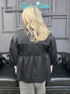 Person wearing a black jacket in a room with gray walls and a neon sign.