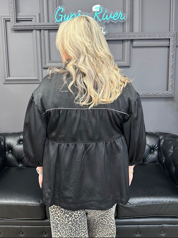 Person wearing a black jacket in a room with gray walls and a neon sign.