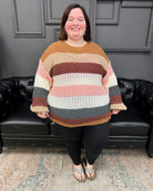 Person wearing a colorful striped sweater standing in a room with a black leather couch and gray walls.