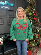 Person wearing a green sweater with a red bow design in front of a decorated Christmas tree.