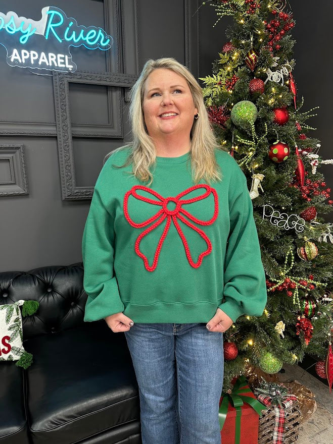Person wearing a green sweater with a red bow design in front of a decorated Christmas tree.