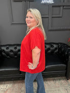 Woman in a red shirt and blue jeans standing in front of a black couch with a Christmas tree and 'Gypsy River Apparel' sign in the background.