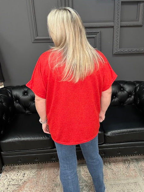 Person wearing a red shirt and blue jeans standing in front of a black leather couch with a Christmas tree and presents in the background.
