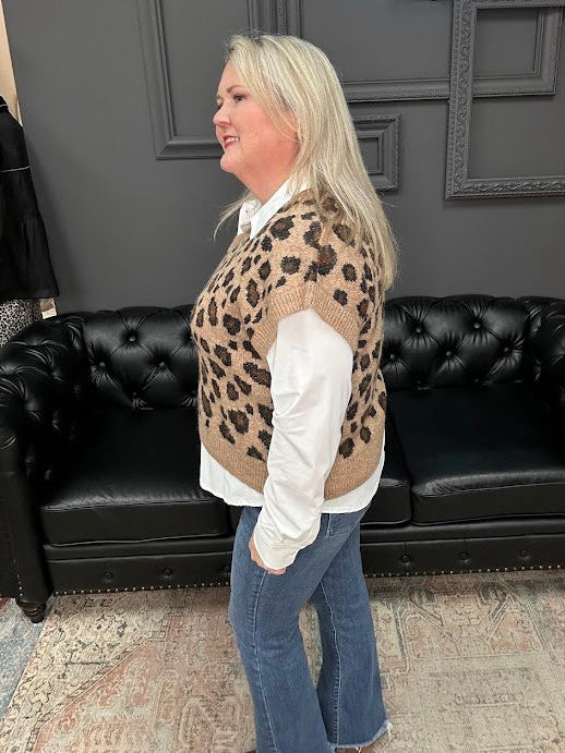 Woman wearing a leopard print vest and blue jeans standing in front of a black leather couch with 'Gypsy River Apparel' branding.