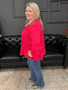 Woman in a red top and blue jeans standing in front of a black leather couch with 'Gypsy River Apparel' branding.