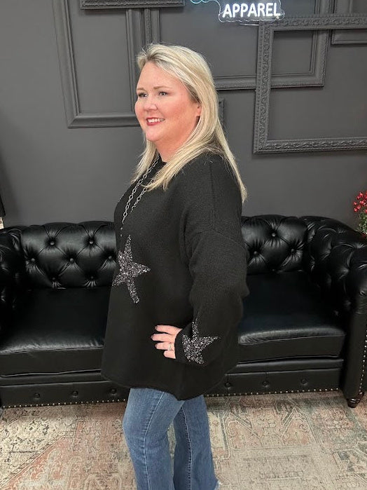 Woman in a black sweater with decorative elements standing in front of a black leather couch and 'Gypsy River Apparel' sign.