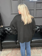Person wearing a black sweater and blue jeans standing in front of a black leather couch.