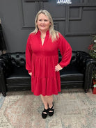 Woman in a red dress standing in front of a black couch and Christmas tree with 'Gypsy River Apparel' sign.