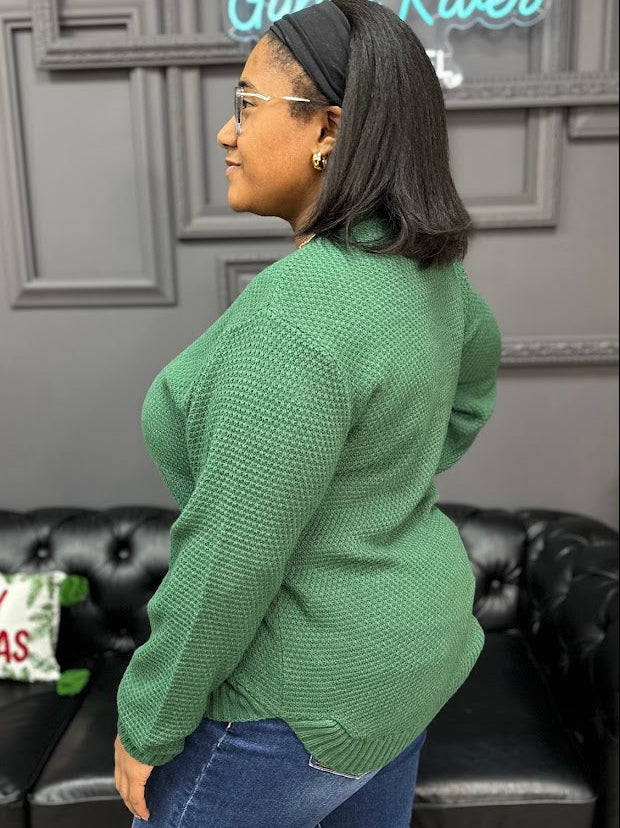 Person wearing a green sweater in a room with a black leather couch and decorative pillows.