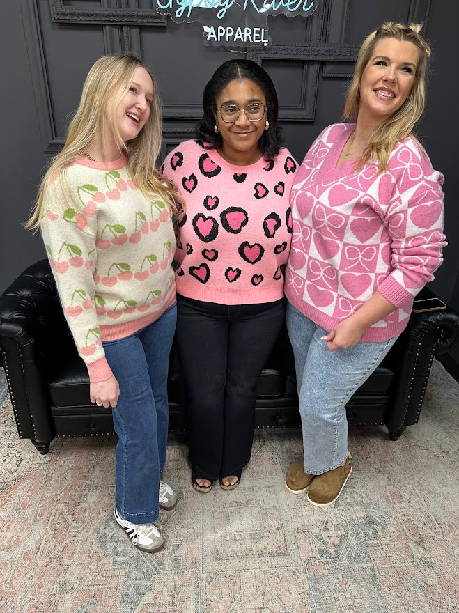 Three women wearing patterned sweaters posing together in a store.