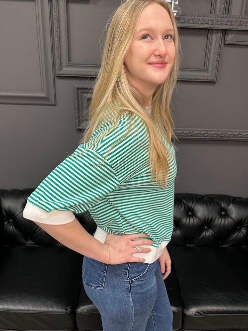 Person wearing a green and white striped shirt and blue jeans standing in front of a black leather couch.