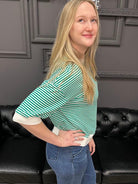 Person wearing a green and white striped shirt and blue jeans standing in front of a black leather couch.