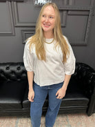 Person wearing a white shirt and blue jeans standing in front of a black leather couch.