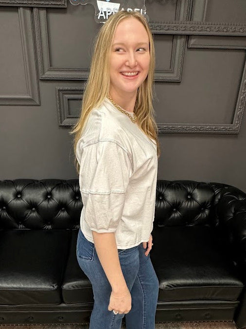 Woman standing in a room with a black leather couch and gray walls.