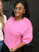 Two women standing close together, one wearing a pink shirt and glasses.