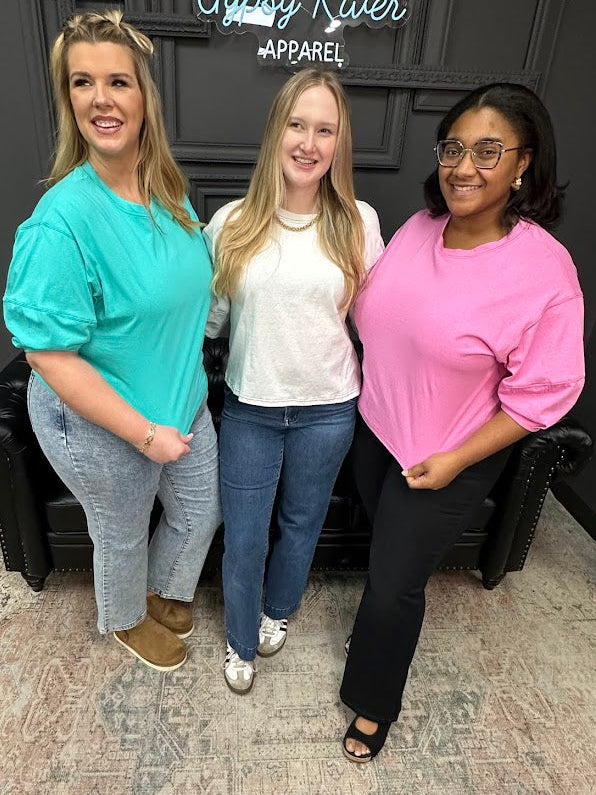 Three women standing together in a room with a black leather couch and a sign in the background.