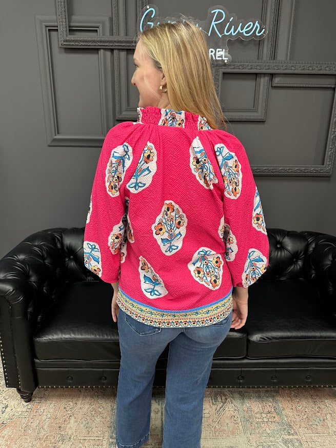 Person wearing a pink blouse with colorful patterns in a room with a black leather couch and gray walls.