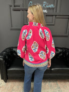 Person wearing a pink blouse with colorful patterns in a room with a black leather couch and gray walls.