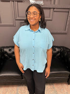 Person wearing a light blue shirt and black pants standing in front of a black leather couch.